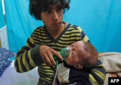 A Syrian boy holds an oxygen mask over the face of an infant at a makeshift hospital following a reported gas attack on the rebel-held besieged town of Douma in the eastern Ghouta region on the outskirts of the capital Damascus, Jan. 22, 2018.