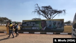 Members of ZANU-PF walk past their party’s poster at a rally in Harare with promises for jobs if President Mnangagwa wins prevails in the election, July 28, 2018. 