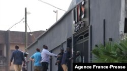 Passers-by walk past policemen standing guard at the entrance of the Livs night-club where a deadly fire occurred in the Bastos district of Yaounde, Jan. 23, 2022.