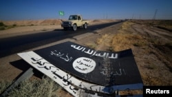 FILE - A black sign belonging to Islamic State militants is seen on the road in Al-Fateha military airport south of Hawija, Iraq, Oct. 2, 2017. Remaining IS fighters in Iraq and Syria are fleeing for parts of Syria controlled by President Bashar al-Assad. 