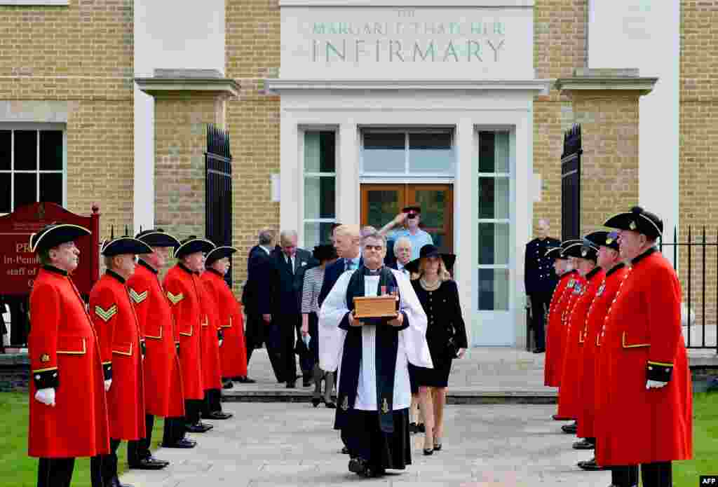 Reverend Richard Whittington carries an oak casket with the ashes of late British former Prime Minister Margaret Thatcher, ahead of her son Mark (L) and his wife Sarah (R) past an honor guard of Chelsea Pensioners after leaving the chapel at the Roya Hospital Chelsea to be laid to rest in the ground.