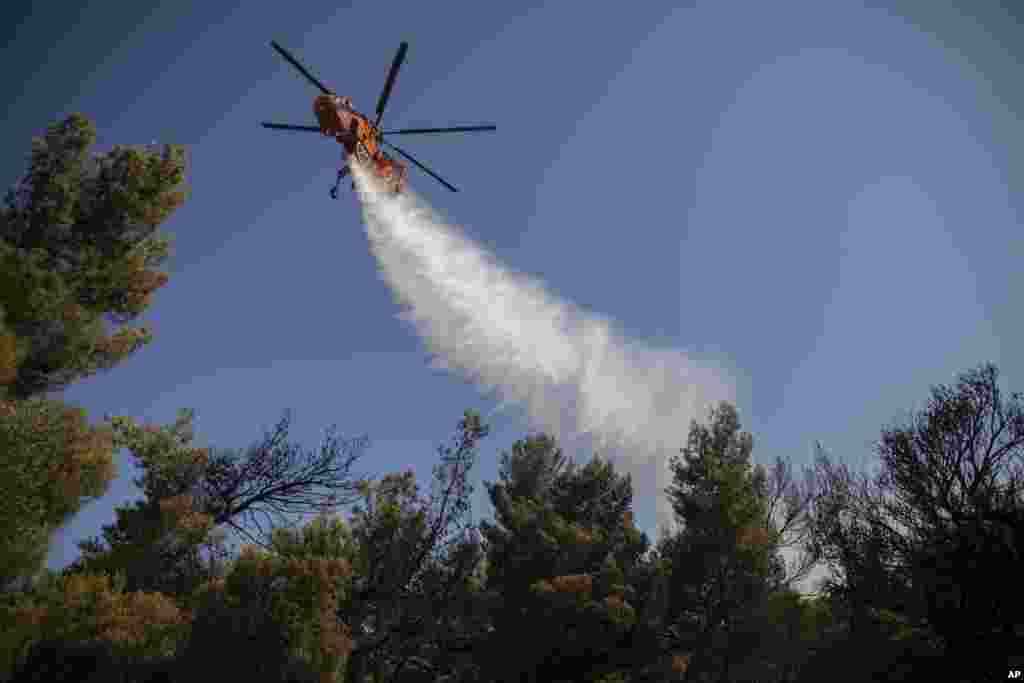 هلیکوپتر آتش&zwnj;نشانی در حال آب پاشیدن به بخشی از آتش در جنگل&zwnj;های حاشیه شهر آتن.&nbsp;