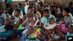 FILE - Women wait to have their children vaccinated against malaria wait at an inoculation site in the Malawi village of Tomali, Dec. 11, 2019.
