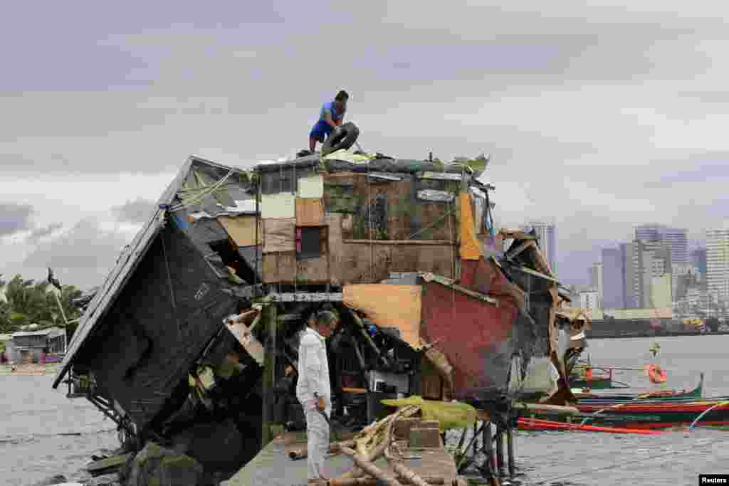 A man works on the roof of his house beside a damaged house after Typhoon Rammasun battered a coastal area of Baseco compound, metro Manila, July 17, 2014. 