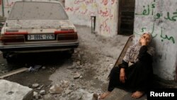 Người đàn bà Palestine ngồi nhìn căn nhà của bà đổ nát vì đạn pháo kích 