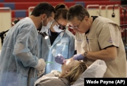 This November 14, 2009 photo shows Dr. Bill Collins, right, working on patient Mendy Johnson as University of Louisville student volunteers Emily Harding, center and Farzan Pouranfar watch during a clinic held by Remote Area Medical.