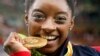United States' Simone Biles bites her gold medal for the artistic gymnastics women's individual all-around final at the 2016 Summer Olympics in Rio de Janeiro, Brazil, Aug. 11, 2016.