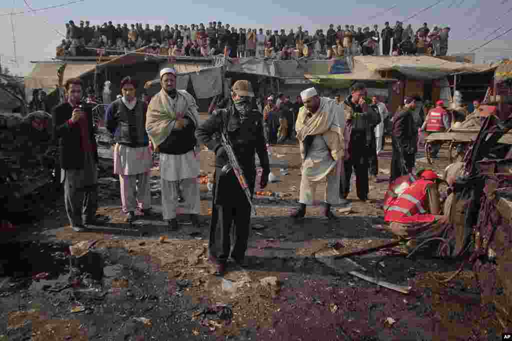 Residents look on as security officials and rescue workers go through the site of a bomb explosion in Jamrud bazaar, about 25 km (15 miles) west of Peshawar in northwest Pakistan, January 10, 2012. (Reuters)