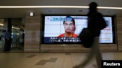 A man walks past screens displaying a television news programme showing an image of Kenji Goto, one of two Japanese citizens taken captive by Islamic State militants, on a street in Tokyo, January 25, 2015.