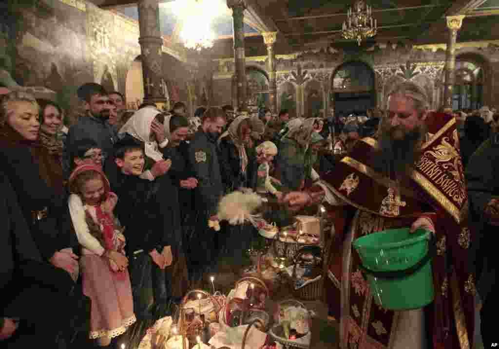 An Orthodox priest blesses traditional Easter cakes and painted eggs prepared for Easter celebrations in the Kyiv-Pechersk Lavra church (Cave Monastery) in the capital city of in Kiev, Ukraine, Sunday, April 20, 2014. (AP Photo/Sergei Chuzavkov)