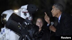 President Barack Obama looks up at the moon as he talks with Agatha Sofia Alvarez-Bareiro, left, a high school senior from the Brooklyn borough of New York, at the second-ever White House Astronomy Night on the South Lawn of the White House in Washington, Oct. 19, 2015.