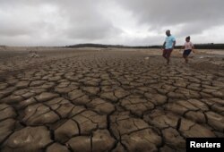 A family negotiates their way through caked mud around a dried up section of the Theewaterskloof dam near Cape Town, South Africa, Jan. 20, 2018.