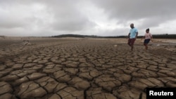 A family negotiates their way through caked mud around a dried up section of the Theewaterskloof dam near Cape Town, South Africa, Jan. 20, 2018.