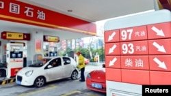 A price board with arrows indicating falling fuel prices is seen as an employee fills the tank of a car at a PetroChina gas station in Hangzhou, Zhejiang province, China, March 26, 2013.