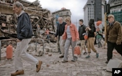 FILE - People walk through debris in the aftermath of a 6.3 magnitude earthquake in Christchurch, New Zealand, Feb. 22, 2011.