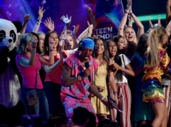 Nick Cannon (tengah) menganugerahkan penghargaan Fandom Choice di acara Teen Choice Awards 2018 kepada ARMY, komunitas penggemar boyband K-Pop BTS (Foto: Chris Pizzello/Invision/AP) .