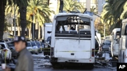 Seorang pria berjalan di dekat bis yang hancur di Tunis (25/11). Presiden Tunisia menyatakan keadaan darurat selama 30 hari di negara itu dan memberlakukan jam malam di ibukota Tunis, menyusul serangan terhadap bus pengawal kepresidenan elit Tunisia yang menewaskan 12 orang.