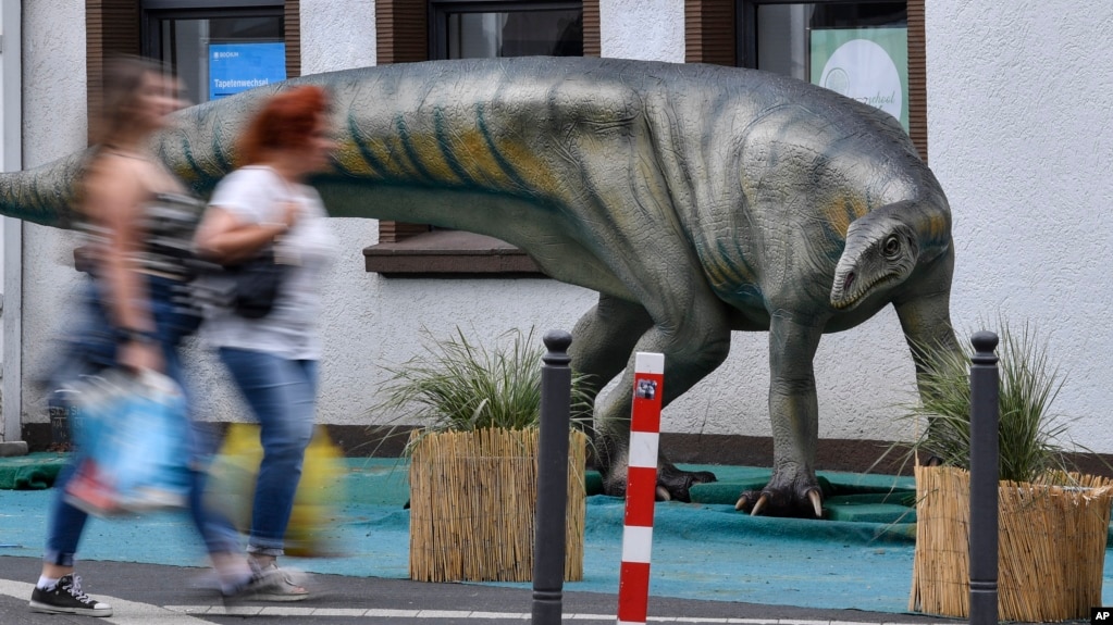 FILE - Pedestrians pass a life-size replica of a Plateosaurus dinosaur in the city center of Bochum, Germany, Monday, Aug. 12, 2019. (AP Photo/Martin Meissner)