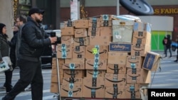 Seorang petugas layanan antar barang mendorong gerobak penuh kotak Amazon di New York City, AS, 14 Februari 2019. (Foto: dok).