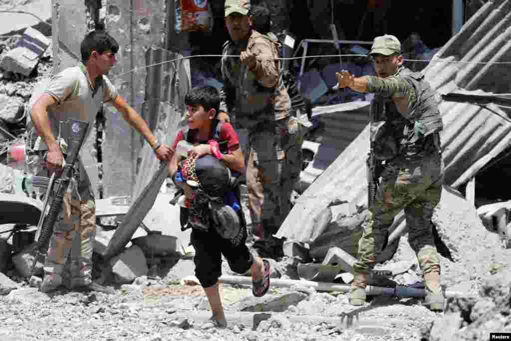 A displaced boy who fled his home walks though Iraqi security forces in al-Zanjili district in western Mosul.