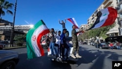 Hundreds of Syrians flash victory signs, honk car horns and wave Syrian, Iranian and Russian flags as they chant slogans against U.S. President Trump in Damascus, Syria, April 14, 2018.