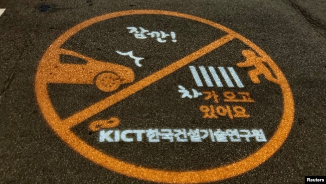 A warning sign is projected next to a zebra crossing in Ilsan, South Korea, March 12, 2019.