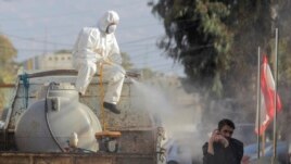 A municipal worker wearing protective gear sprays disinfectant as a precaution against the coronavirus outbreak as a man speaks on his mobile phone, in the suburb of Beir Hassan, Beirut, Lebanon, Monday, March 16, 2020. (AP Photo/Hassan Ammar)