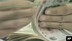 A bank teller counts a stack of US and Chinese currency.