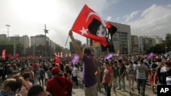 ຊາຍຄົນນຶ່ງໂບກທຸງ ທີ່ມີຮູບຂອງທ່ານKemal Ataturk ຜູ້ສ້າງຕັ້ງປະເທດເທີກີ ໃນຂະນະທີ່ຊາວໜຸ່ມຫລາຍພັນຄົນ ໄປເຕົ້າໂຮມກັນຢູ່ທີ່ຈະຕຸລັດ Kizilay ນະຄອນ Ankara, ໃນວັນທີ 2 ມິຖຸນາ 2013.