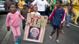 A young girl with a placard showing the face of Nelson Mandela and referring to his clan name "Madiba", marches with others to celebrate his life, in the street outside his old house in Soweto, Johannesburg, South Africa, Dec. 6, 2013. 