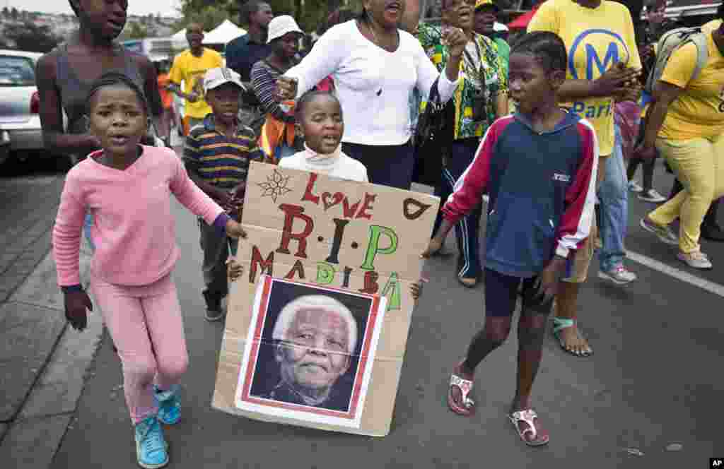 A young girl with a poster of Nelson Mandela marches with others to celebrate his life, in the street outside his old house in Soweto, Johannesburg, Dec. 6, 2013. 