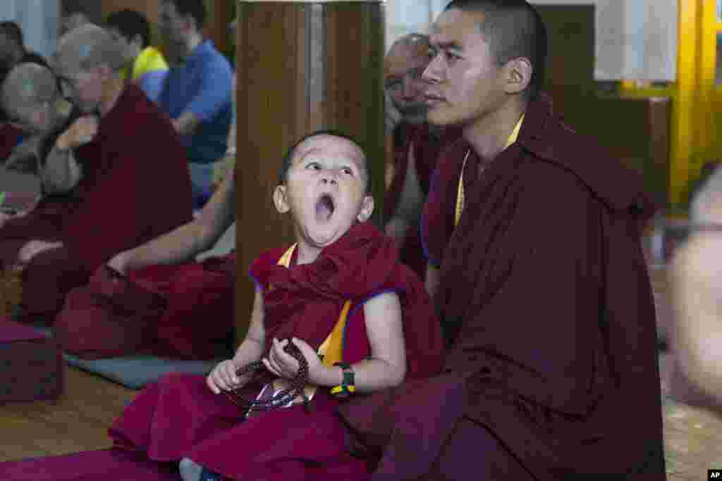 A novice Tibetan Buddhist monk yawns as he sits on the lap of an older monk during a religious talk by their spiritual leader the Dalai Lama at the Tsuglakhang temple in Dharmsala, India.