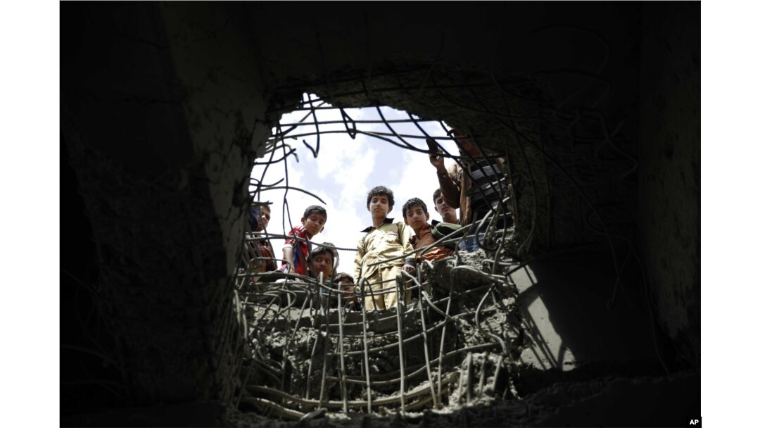 FILE - Boys look through a hole made by a Saudi-led airstrike on a bridge in Sanaa, Yemen, March 23, 2016.