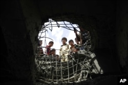 FILE - Boys look through a hole made by a Saudi-led airstrike on a bridge in Sanaa, Yemen, March 23, 2016.