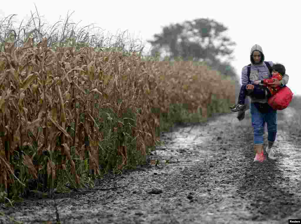 Migran menggendong seorang anak laki-laki dalam perjalanan dekat kota Sid, Serbia, menuju perbatasan ke Kroasia.