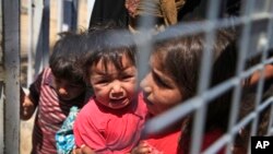 A Syrian child carries a baby crying while they wait with others to cross back to the border town of Tal Abyad in Syria from Turkey, at the border crossing in Akcakale, southeastern Turkey, June 17, 2015. 
