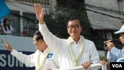 Opposition leader Sam Rainsy (white shirt, right), and deputy opposition leader Kem Sokha (left) wave to people watching the march in Phnom Penh, Dec. 29, 2013. (R. Carmichael/VOA)