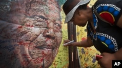 A well-wisher writes a message on a poster of Nelson Mandela on which she and others have written their messages of condolence and support, in the street outside his old house in Soweto, Johannesburg, South Africa, Dec. 6, 2013.