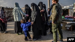 FILE - Veiled women, reportedly wives and members of the Islamic State, walk under the supervision of a fighter from the Syrian Democratic Forces at the al-Hol camp in al-Hasakah governorate in northeastern Syria, Feb. 17, 2019.