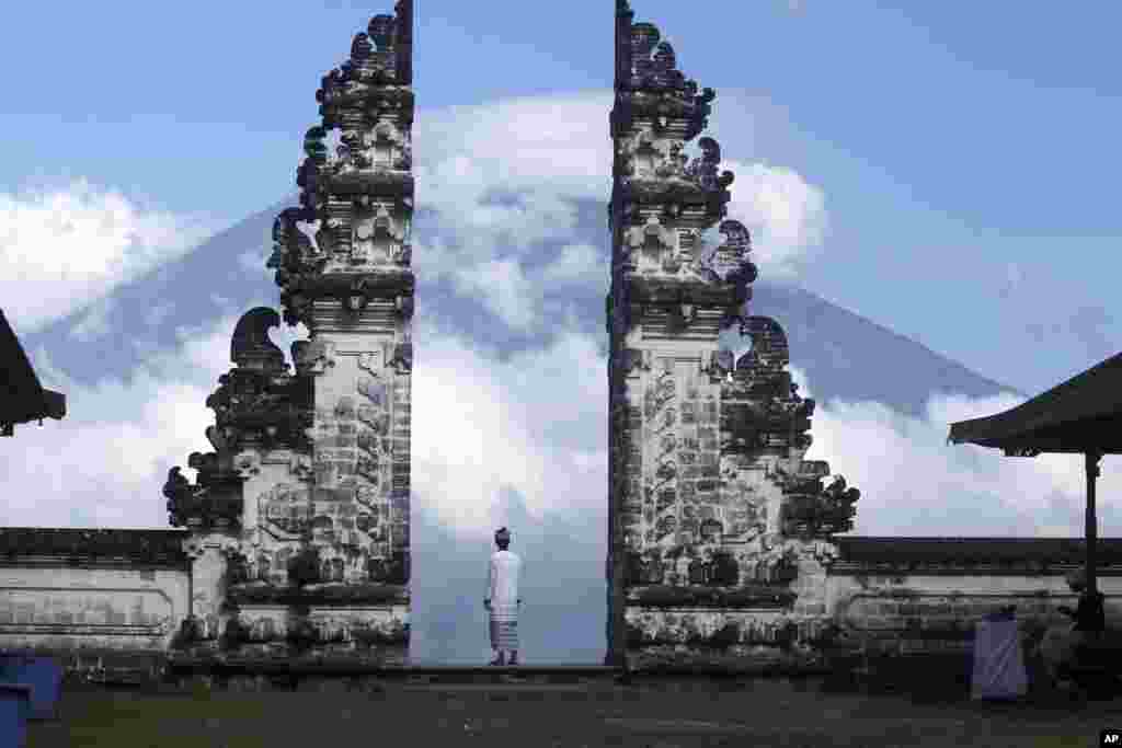 Balinese man watches Mount Agung volcano at a temple in Karangasem, Bali, Indonesia.