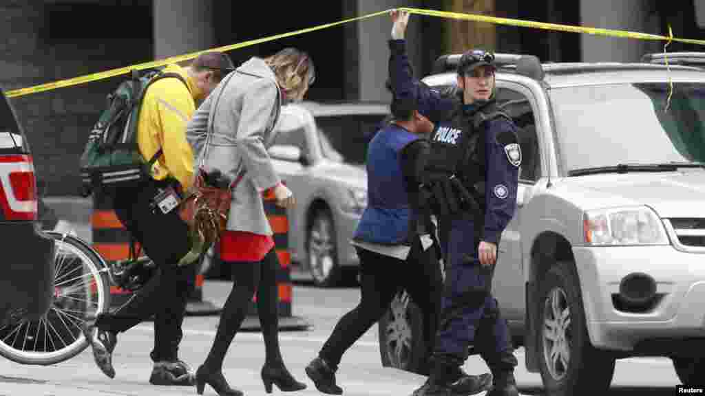 Un agent de la police d&#39;Ottawa soulève le ruban de sécurité pour laisser les piétons quitter le centre-ville après une fusillade à Ottawa, le 22 Octobre 2014. REUTERS/Blair Gable 