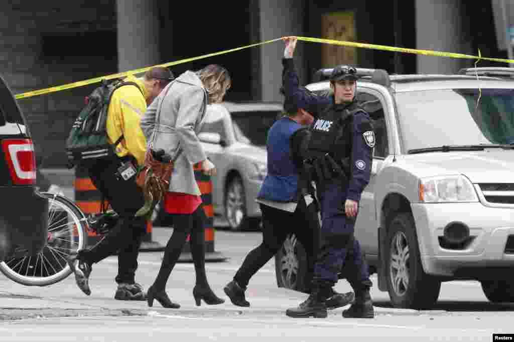 A police officer holds up a length of police tape for pedestrians leaving the downtown area following shooting incidents in Ottawa.