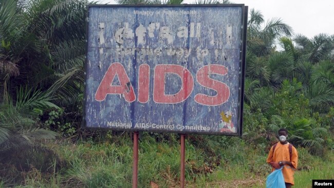 FILE - A man stands next to an AIDS billboard as he cleans a street in Yaounde, Cameroon, March 20, 2009.