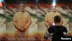 FILE - A man uses his mobile phone to take photos of a poster for the now delayed film "PM Narendra Modi" in Mumbai, India, Jan. 7, 2019.
