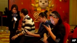 FILE - In this photo taken Feb. 2, 2015, a woman browses her smartphone near other attendees at a press conference in Beijing. Chinese mobile video applications, such as Ingkee, are similar to Twitter’s Periscope and Facebook Live, and allow streamers to distribute live video and simultaneously interact with viewers.