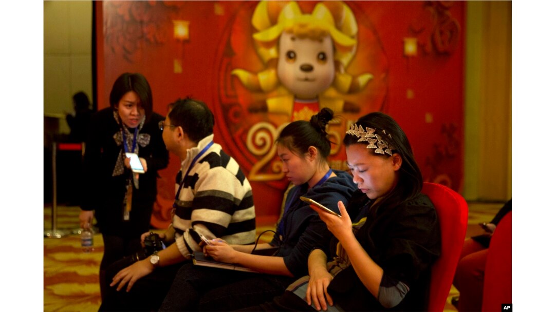FILE - In this photo taken Feb. 2, 2015, a woman browses her smartphone near other attendees at a press conference in Beijing.