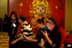FILE - In this photo taken Feb. 2, 2015, a woman browses her smartphone near other attendees at a press conference in Beijing.