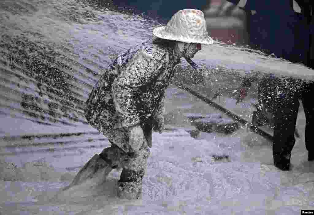 A firefighter is covered with Aqueous Film Forming Foam (AFFF) as he tries to control a fire that broke out in a manufacturing plant on the outskirts of Ahmedabad, India.