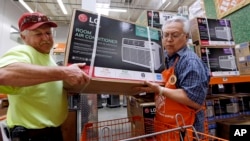 FILE - Store greeter Danny Olivar, right, lends a hand to a customer who bought an air-conditioning unit at a Home Depot store in Seattle, Aug. 1, 2017. Home Depot made more in profit from May through July than in any other quarter in its history.