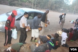 Clifford Oluoch (right) distributes bread to homeless children with the help of volunteers. (VOA/Rael Ombuor)